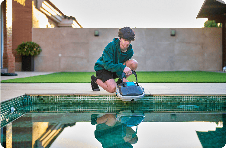 Person setting pool cleaning robot beside water.